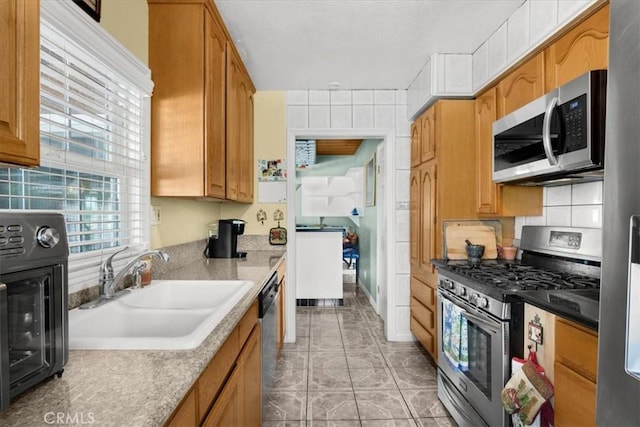 kitchen with light tile patterned floors, decorative backsplash, brown cabinets, stainless steel appliances, and a sink