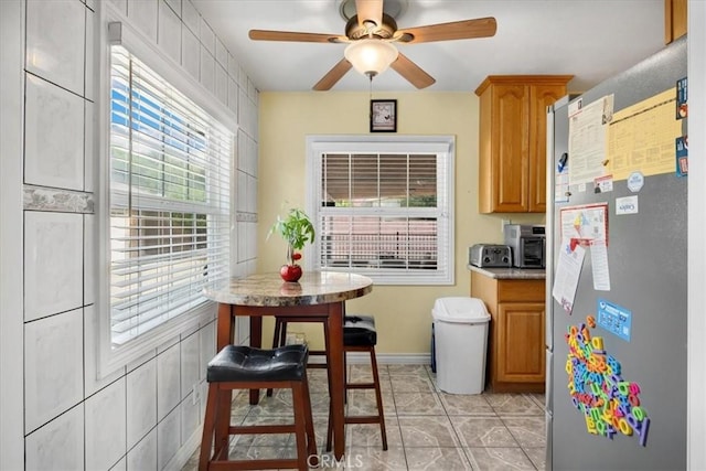 kitchen featuring a toaster, ceiling fan, freestanding refrigerator, light countertops, and light tile patterned flooring