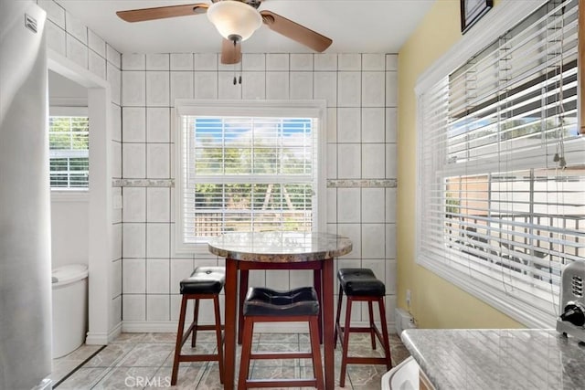 dining room featuring light tile patterned floors, tile walls, and a ceiling fan