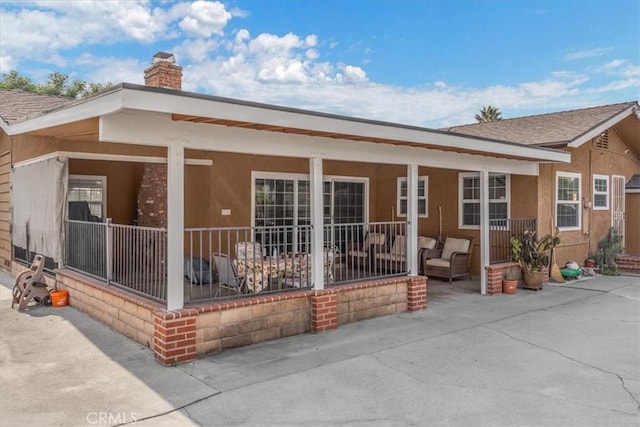 back of property with roof with shingles, a patio, a chimney, and stucco siding