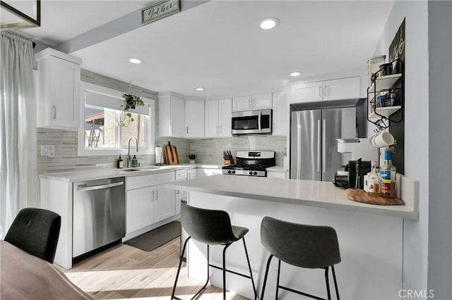 kitchen featuring a breakfast bar, a sink, stainless steel appliances, a peninsula, and white cabinets