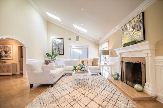 living room with a premium fireplace, a skylight, wainscoting, crown molding, and a decorative wall