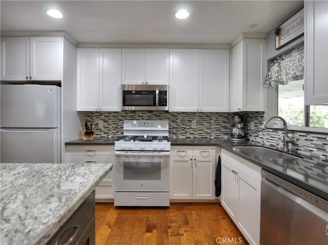 kitchen featuring tasteful backsplash, wood finished floors, stainless steel appliances, white cabinetry, and a sink