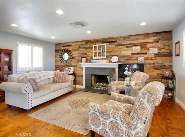 living room with visible vents, a tile fireplace, wood finished floors, wood walls, and recessed lighting