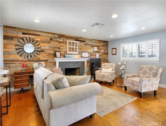 living area featuring wooden walls, visible vents, wood finished floors, a fireplace, and recessed lighting