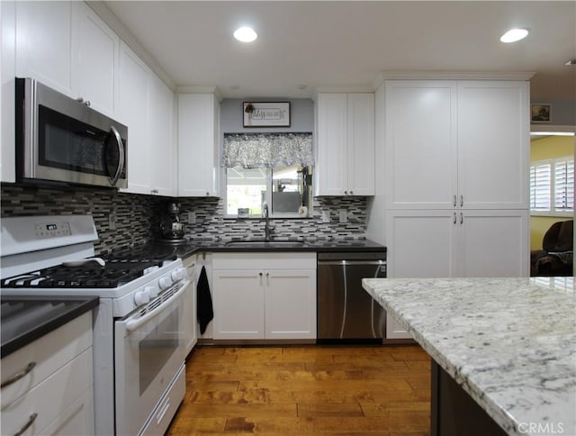 kitchen with stainless steel appliances, white cabinetry, a sink, wood finished floors, and plenty of natural light