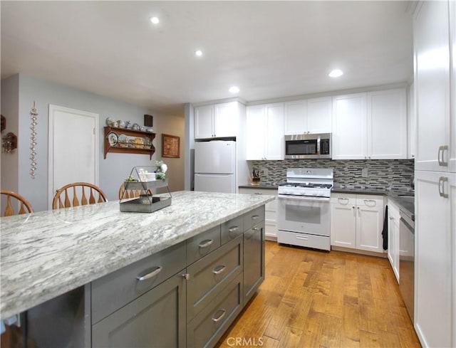 kitchen featuring light stone counters, light wood-style flooring, white appliances, white cabinets, and backsplash