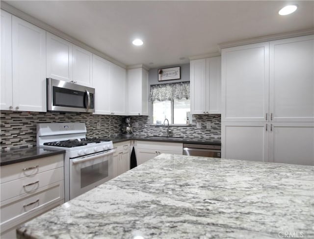 kitchen with a sink, white cabinets, appliances with stainless steel finishes, dark stone counters, and tasteful backsplash