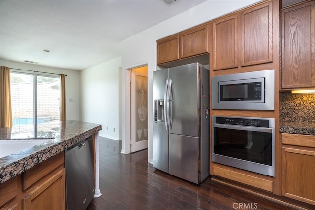 kitchen with appliances with stainless steel finishes, brown cabinetry, decorative backsplash, baseboards, and dark wood-style flooring