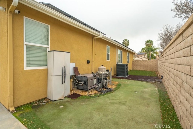 back of property with central air condition unit, stucco siding, a lawn, and fence