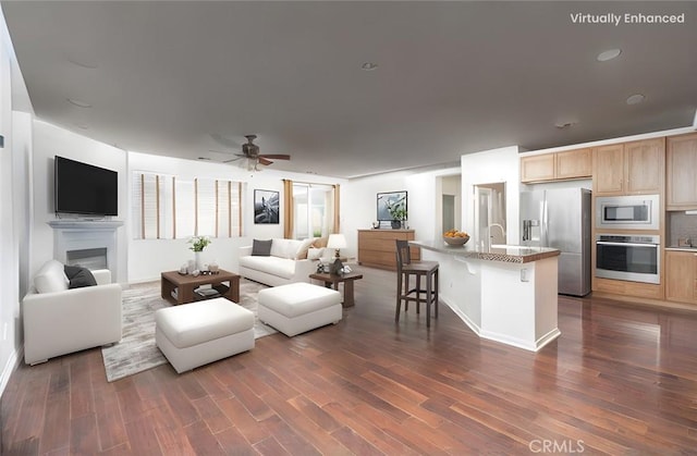 living room with dark wood finished floors, a glass covered fireplace, baseboards, and a ceiling fan