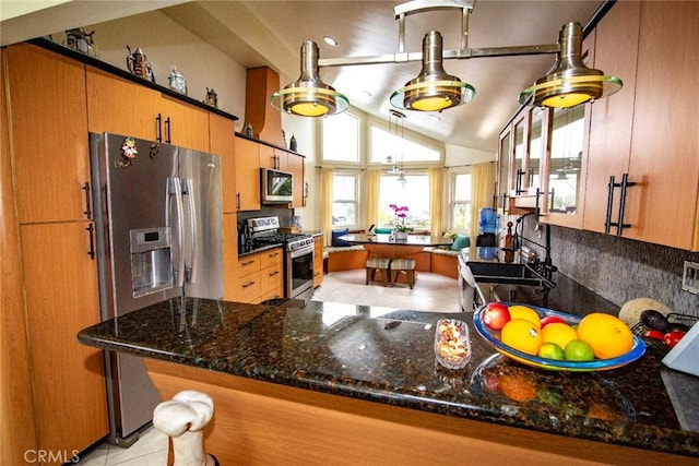 kitchen featuring stainless steel appliances, a sink, vaulted ceiling, tasteful backsplash, and brown cabinetry