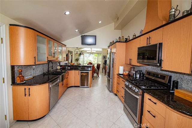 kitchen with lofted ceiling, appliances with stainless steel finishes, a sink, dark stone counters, and a peninsula