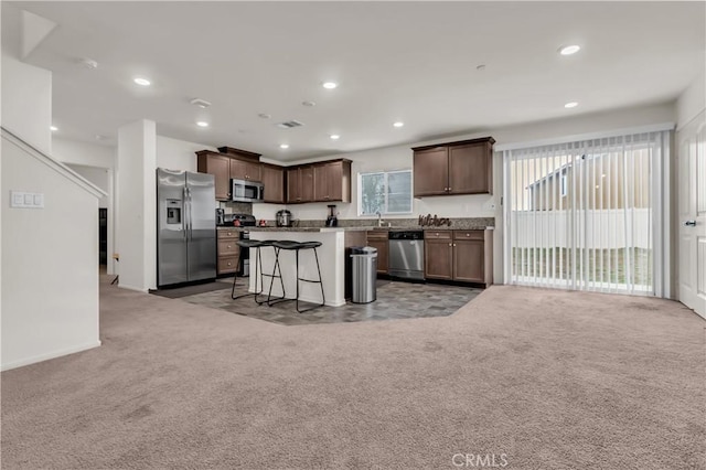 kitchen featuring open floor plan, light carpet, a kitchen breakfast bar, stainless steel appliances, and a sink