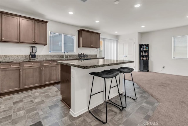 kitchen featuring a sink, dark stone counters, light carpet, and a breakfast bar area