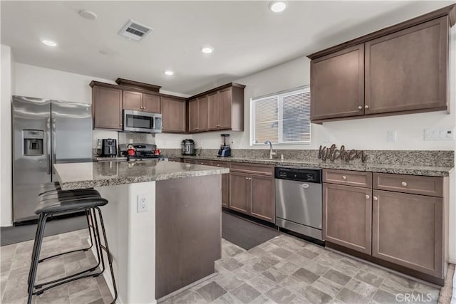 kitchen featuring visible vents, a breakfast bar, a center island, stainless steel appliances, and stone counters