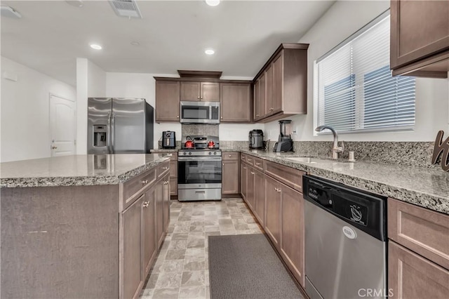 kitchen with light stone counters, visible vents, a sink, stone finish floor, and appliances with stainless steel finishes