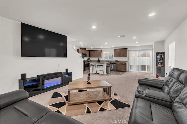 living area featuring light carpet, visible vents, recessed lighting, and a glass covered fireplace