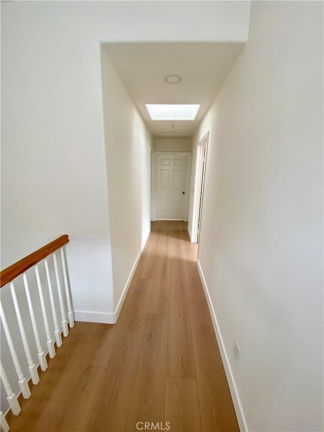 hall featuring a skylight, baseboards, and light wood-type flooring