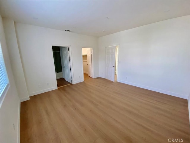 unfurnished bedroom with a spacious closet, visible vents, baseboards, light wood-type flooring, and a closet