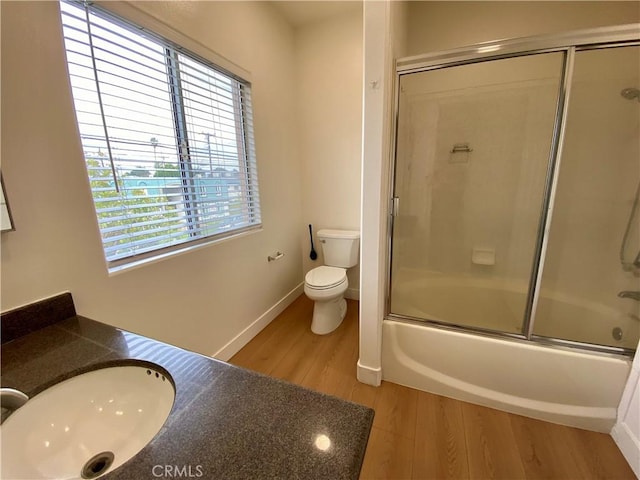 bathroom with vanity, wood finished floors, baseboards, shower / bath combination with glass door, and toilet