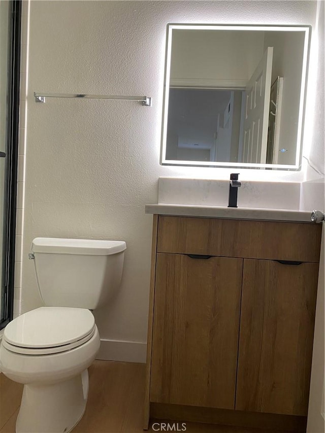 full bathroom featuring vanity, baseboards, an enclosed shower, toilet, and a textured wall