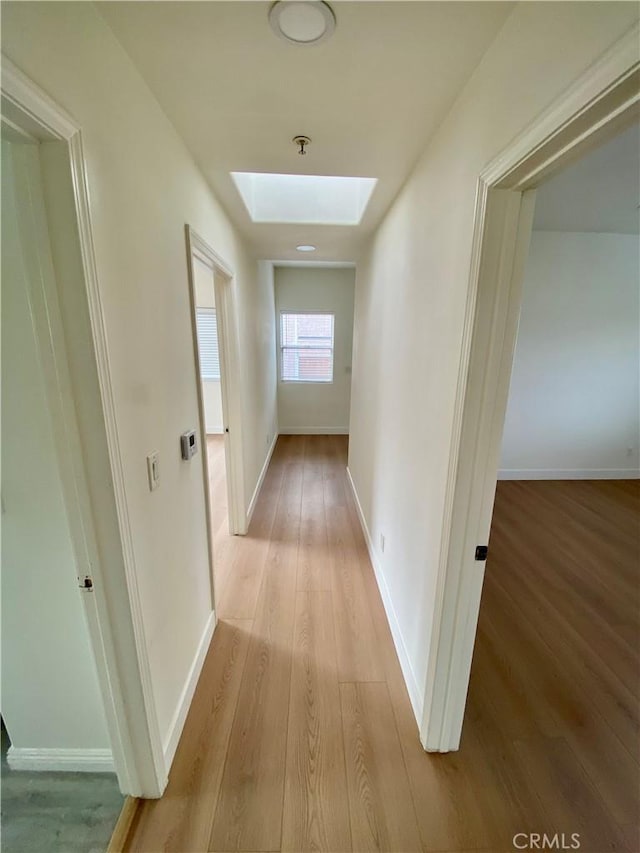 corridor featuring a skylight, wood finished floors, and baseboards