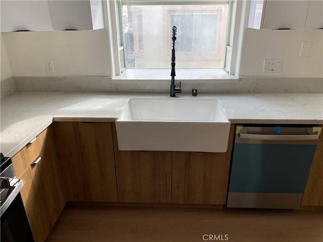 kitchen featuring light wood-style flooring, stainless steel dishwasher, brown cabinetry, modern cabinets, and a sink