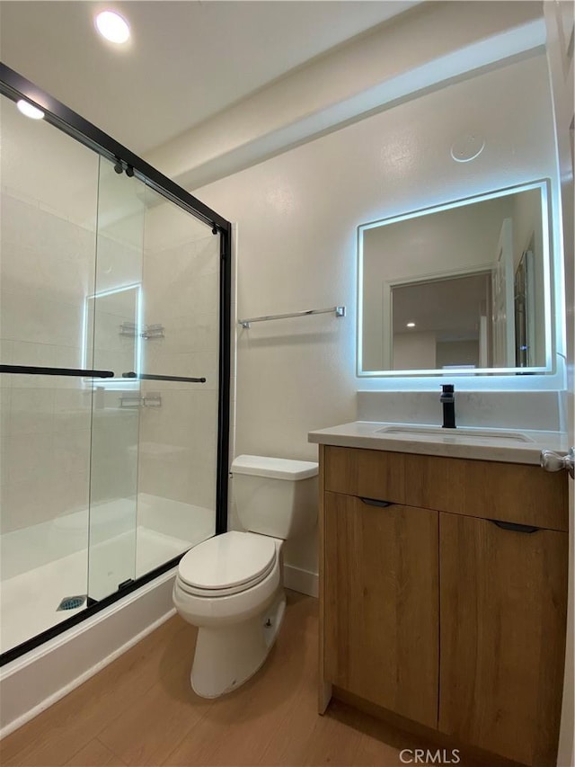 bathroom with wood finished floors, toilet, a stall shower, and vanity