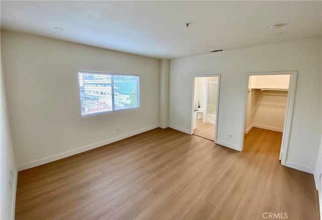 unfurnished bedroom featuring visible vents, light wood-style flooring, a closet, baseboards, and a spacious closet