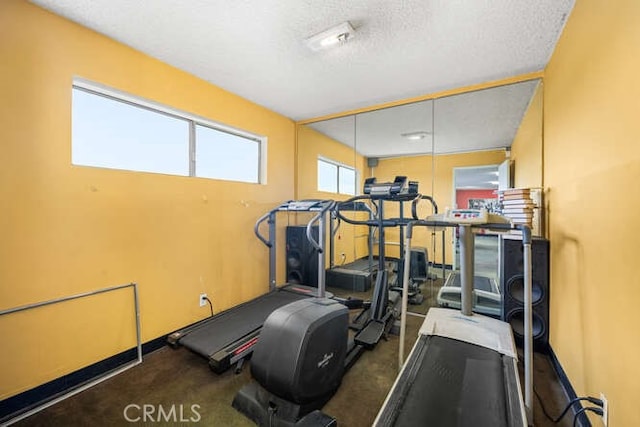 workout area featuring baseboards, a textured ceiling, and carpet