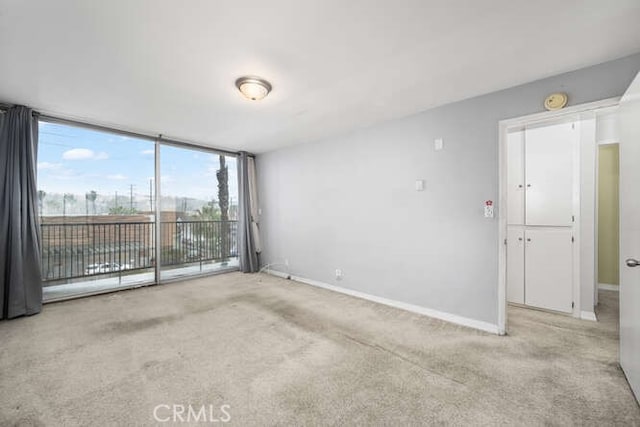 spare room with light colored carpet, a wall of windows, and baseboards