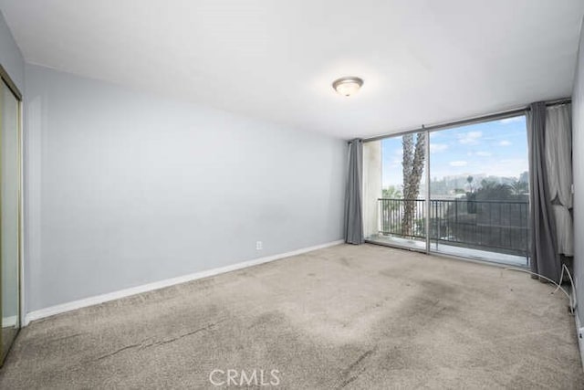 carpeted empty room featuring a wall of windows and baseboards