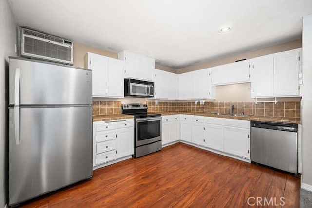 kitchen with a sink, tile counters, an AC wall unit, white cabinets, and appliances with stainless steel finishes