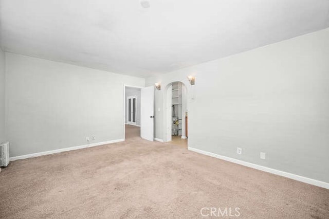 carpeted empty room featuring arched walkways and baseboards