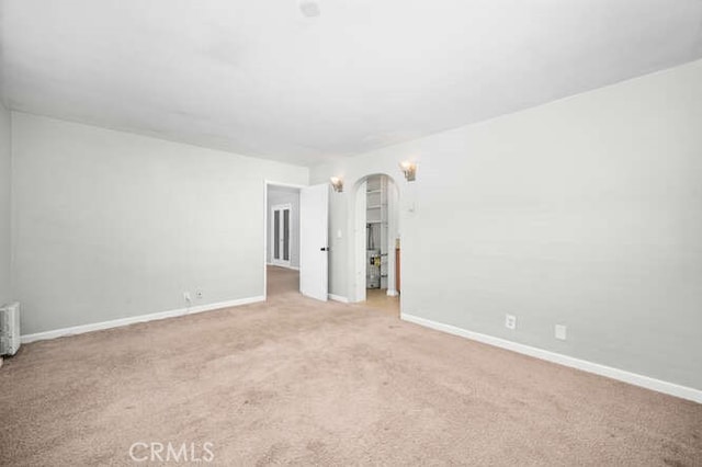empty room featuring baseboards, arched walkways, and carpet