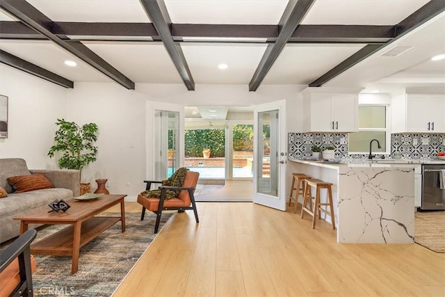 interior space with white cabinetry, light wood-type flooring, stainless steel dishwasher, tasteful backsplash, and a kitchen bar