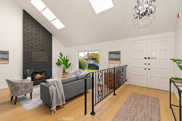 living area with baseboards, high vaulted ceiling, light wood-style flooring, a brick fireplace, and a notable chandelier