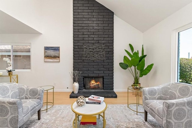 living room with a brick fireplace, wood finished floors, baseboards, and vaulted ceiling