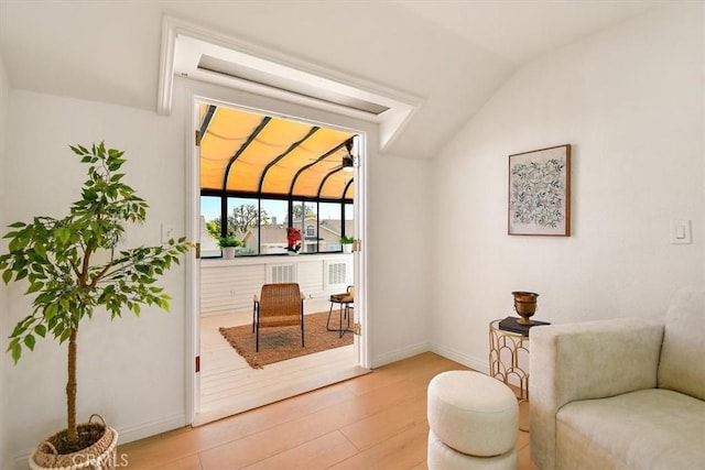 living area with light wood finished floors, a sunroom, baseboards, and vaulted ceiling