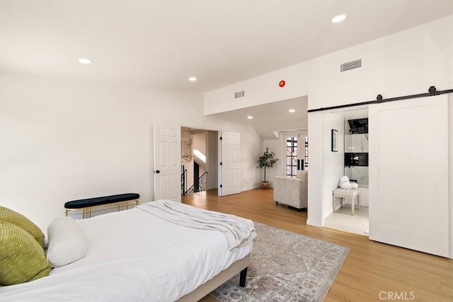 bedroom with visible vents, recessed lighting, a barn door, light wood finished floors, and vaulted ceiling