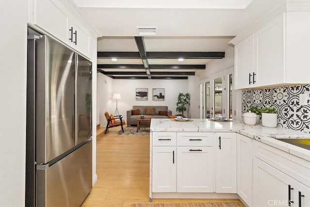 kitchen with light wood finished floors, a peninsula, freestanding refrigerator, white cabinetry, and beamed ceiling