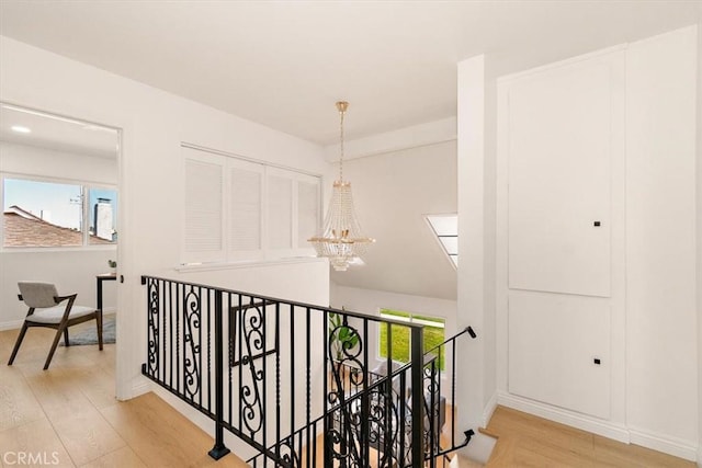 hallway with baseboards, an upstairs landing, an inviting chandelier, and wood finished floors