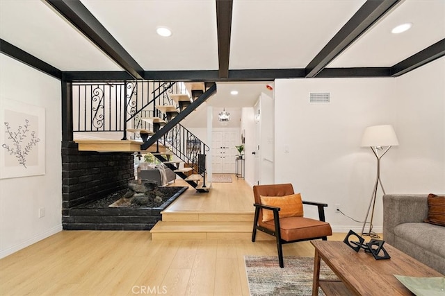 living area with visible vents, beamed ceiling, wood finished floors, and stairs