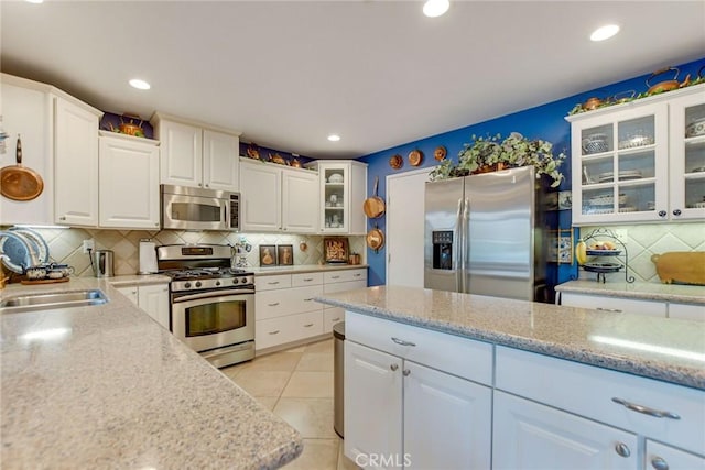 kitchen featuring a sink, appliances with stainless steel finishes, white cabinets, light tile patterned floors, and decorative backsplash