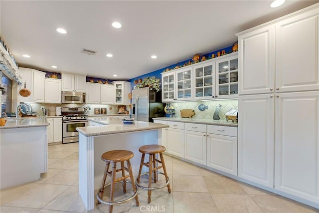 kitchen featuring stainless steel appliances, visible vents, light tile patterned flooring, and a center island