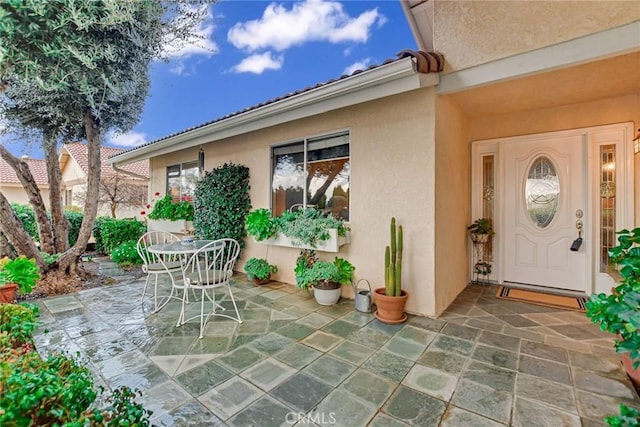 property entrance featuring a tiled roof, outdoor dining area, a patio area, and stucco siding