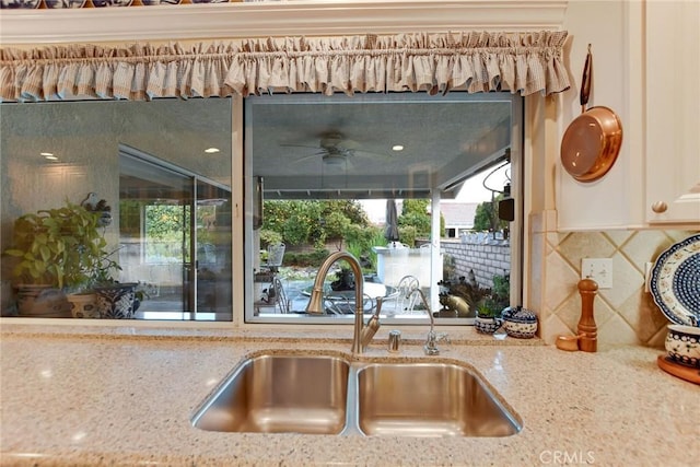 kitchen featuring a sink, light stone countertops, backsplash, and a ceiling fan