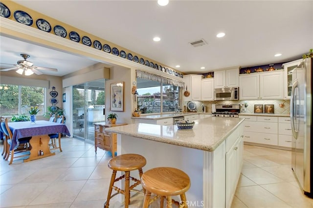 kitchen featuring light stone counters, visible vents, a kitchen island, appliances with stainless steel finishes, and backsplash