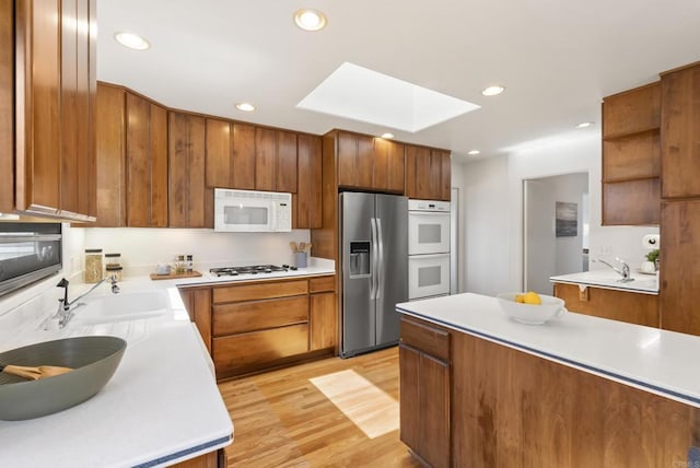 kitchen with light wood finished floors, light countertops, a skylight, brown cabinetry, and white appliances